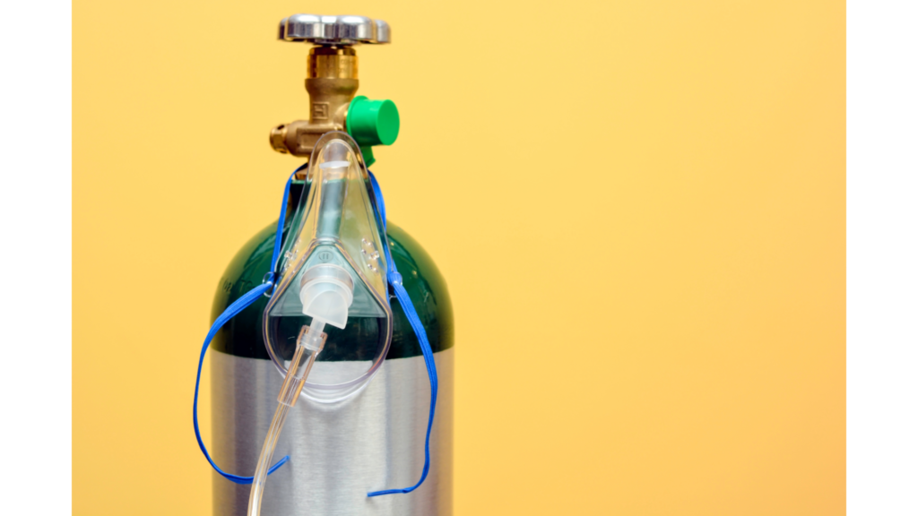 Imagem de cilindro de oxigênio medicinal com máscara facial acoplada para oxigenoterapia. Equipamento utilizado no tratamento de hipoxemia, insuficiência respiratória e suporte em atendimentos hospitalares e domiciliares.